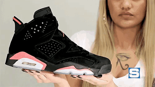 a woman is holding a pair of black and pink shoes with the letter s on her chest