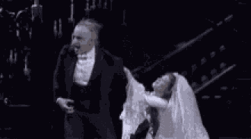 a black and white photo of a man in a tuxedo and a woman in a white dress .