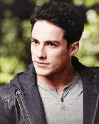 a man wearing a grey shirt and a black jacket looks at the camera