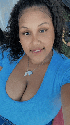 a woman wearing a blue shirt and a necklace with an angel wing pendant smiles for the camera