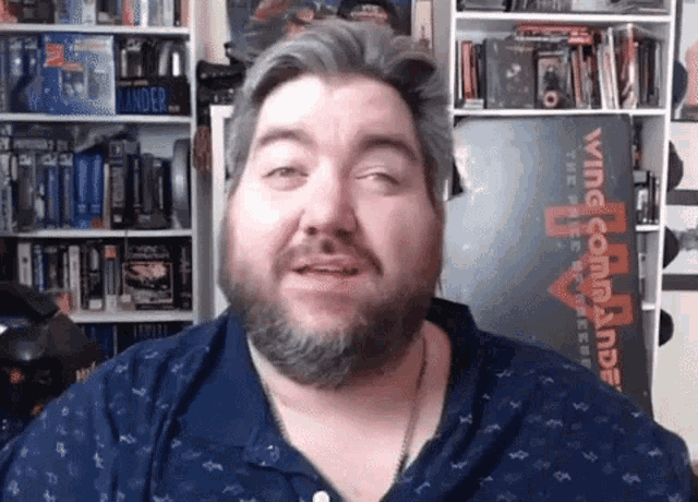 a man with a beard is looking at the camera in front of a wing commander poster