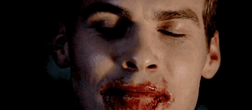 a close up of a vampire 's face with red eyes and blood on his mouth .