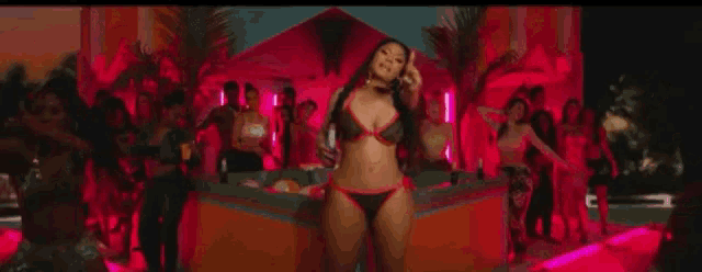 a woman in a bikini is standing in front of a crowd of people with the words ratatata written in pink .