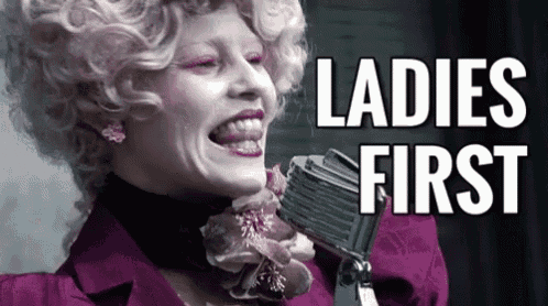 a woman is singing into a microphone with the words ladies first written above her .