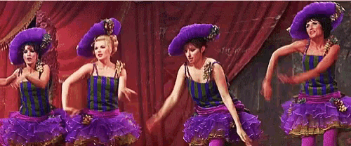 a group of women in purple dresses and hats are dancing on stage .