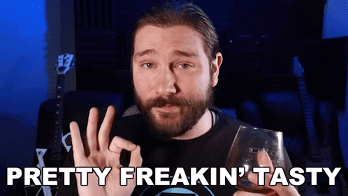 a man with a beard is holding a glass of whiskey and says pretty freakin tasty