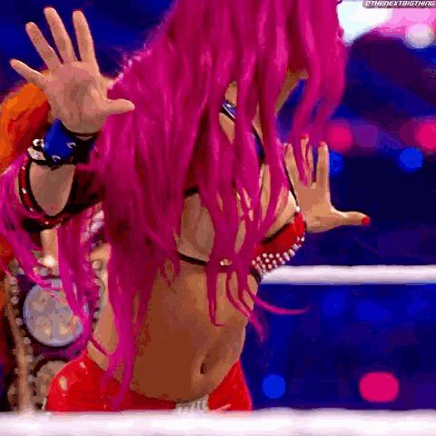 a woman with pink hair is standing in a wrestling ring with her hands outstretched .