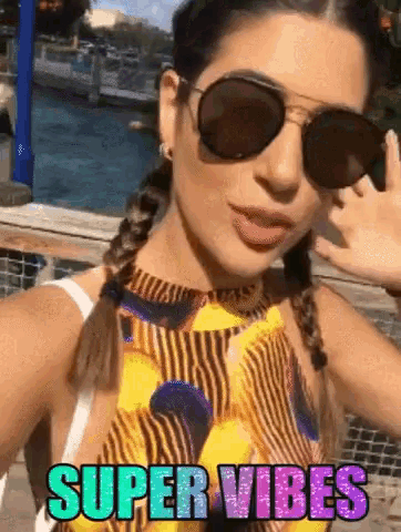 a woman wearing sunglasses takes a selfie with the words super vibes in the background