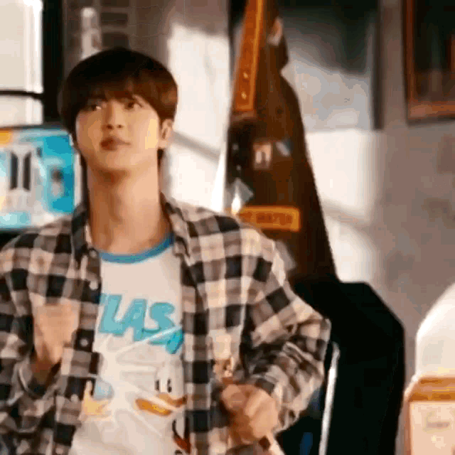 a young man in a plaid shirt is standing in a room holding a guitar .