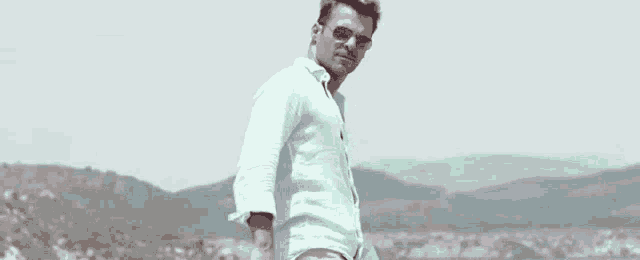 a man wearing sunglasses and a light blue shirt is standing on a hill .