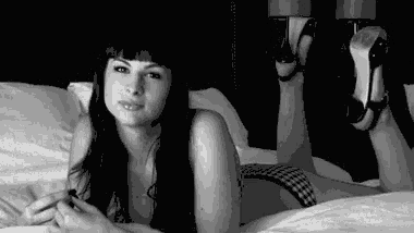 a black and white photo of a woman laying on a bed smoking a cigarette .