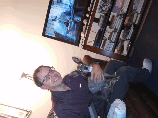 a man is holding a small dog in front of a flat screen tv