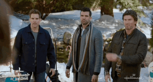 three men are standing in the snow in front of a sign that says hallmark on it