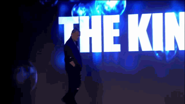 a man stands in front of a large screen that says " the kin "
