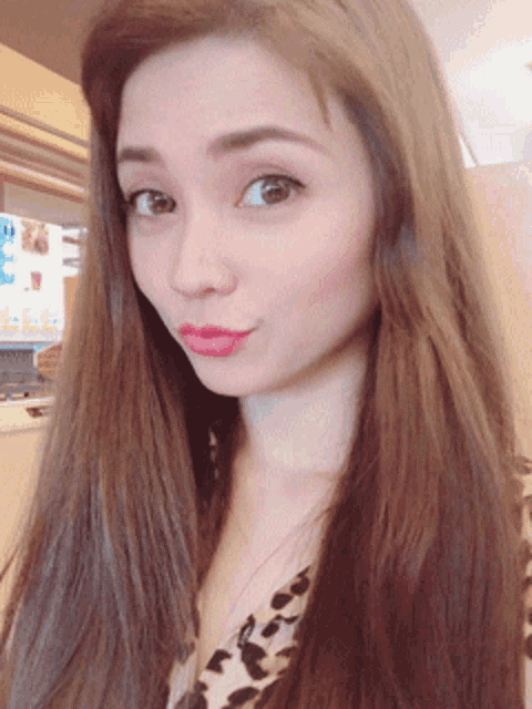 a woman with long brown hair and a leopard print shirt looks at the camera