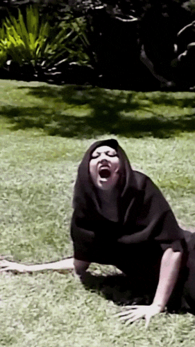 a person in a black robe is laying on the grass with their mouth open