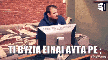 a man sitting on a couch looking at a computer screen with the words ti byzia einai ayta pe