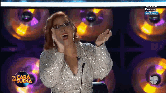 a woman in a sequined top is sitting in front of a microphone and a sign that says tu cara me suena