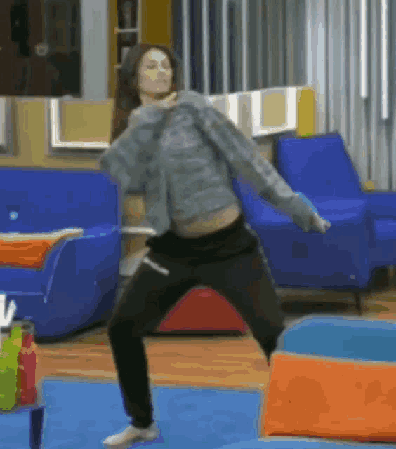 a woman is dancing in a living room with a blue couch in the background