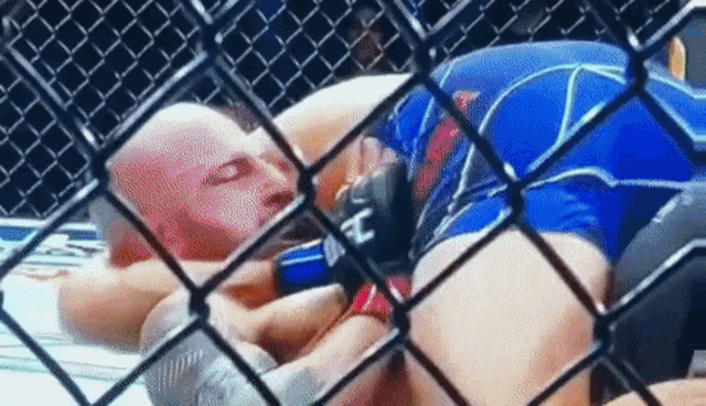 a man is laying on the ground in a cage while another man is wrestling him .