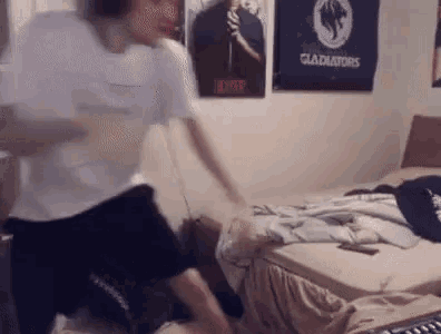 a man is sitting on the floor in front of a bed with posters on the wall .