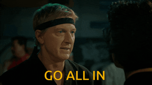 a man wearing a headband talks to another man in front of a sign that says " go all in "