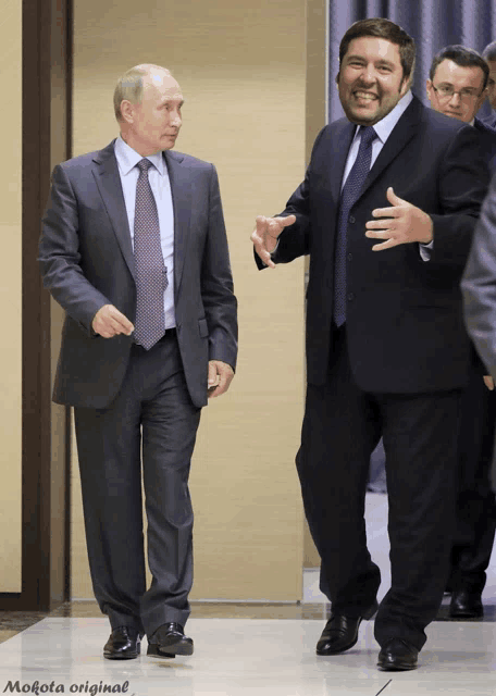a man in a suit and tie talks to another man in a black suit and tie
