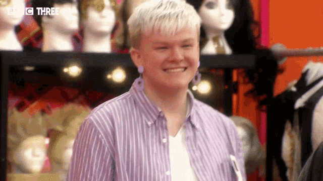 a young man wearing a striped shirt and earrings is smiling in front of a mannequin .