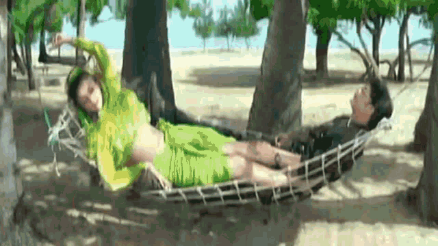 a man and woman are laying in a hammock on a beach .