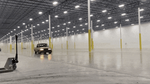 a car is driving through an empty warehouse with a forklift in the background