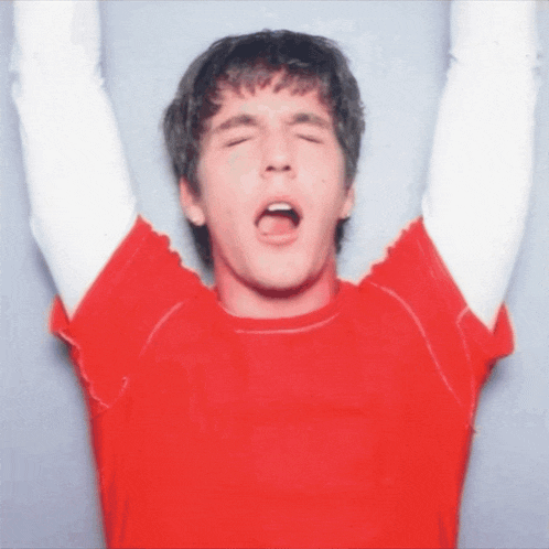 a man in a red shirt is screaming with his arms in the air