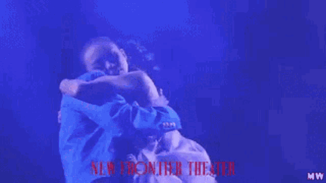 a man in a blue shirt is hugging a woman in a white dress in front of a sign that says new frontier theater
