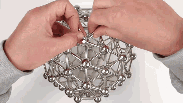 a person is playing with a metal toy that looks like a chemical structure