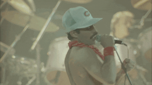 a man in a white hat and shorts is singing into a microphone on a stage