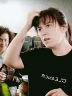 a woman wearing a black shirt that says ' я3иа3jo ' on it scratches her head