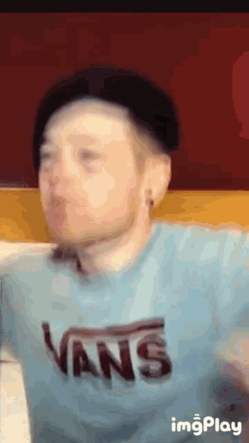 a man wearing a vans shirt and a black hat