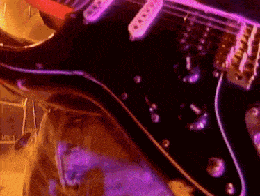 a close up of an electric guitar with purple lights behind it