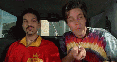 a man wearing a tie dye shirt with a crown on it sits next to another man