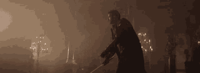 a man in a black coat is holding a sword in a dark room .