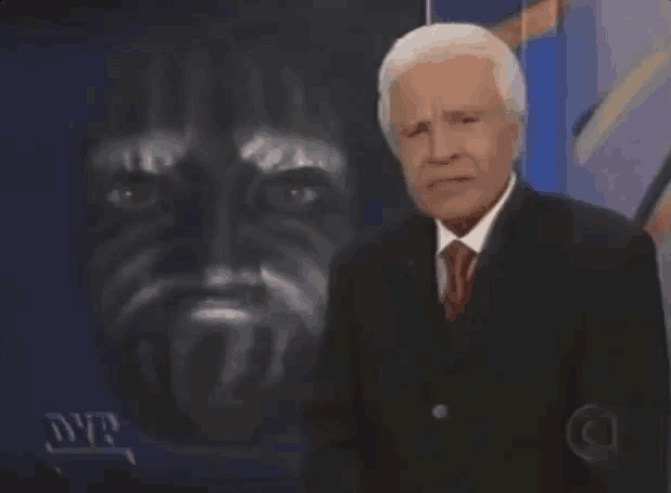 a man in a suit and tie stands in front of a painting of a man 's face
