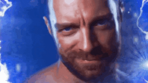 a shirtless man with a beard is looking at the camera with a blue background behind him .
