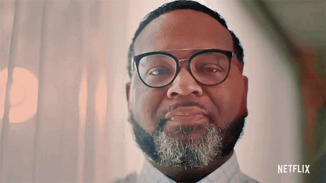 a man with glasses and a beard has a netflix logo on the bottom right