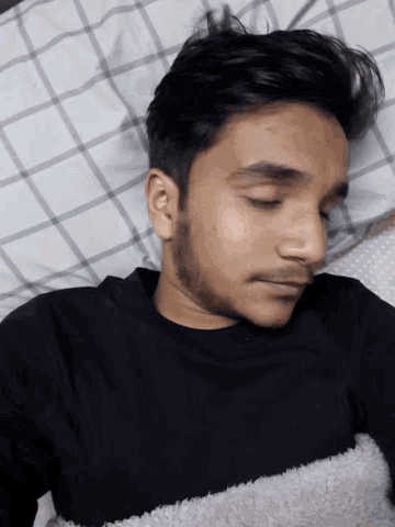a man in a black shirt is sleeping on a bed with plaid sheets