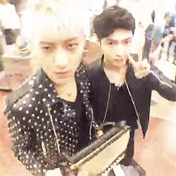 two young men are standing next to each other in a room and one is holding a purse .