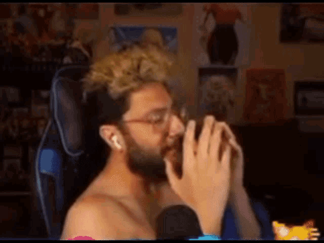 a shirtless man with a beard is sitting in a chair with his hands folded in front of his face .