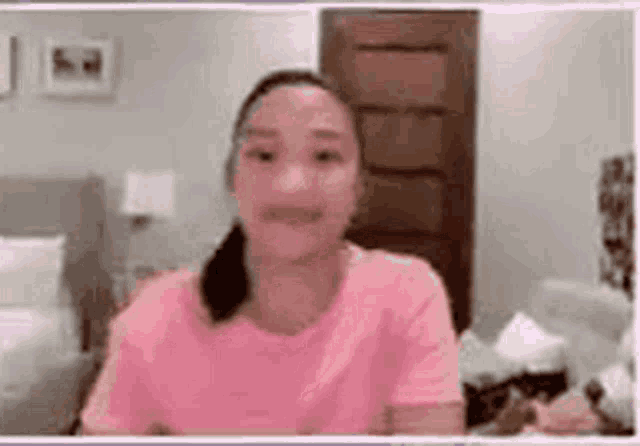 a woman in a pink shirt is sitting on a couch and smiling .