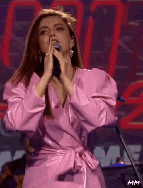a woman in a pink dress singing into a microphone with mm written on the bottom right