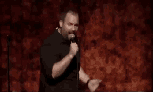 a man is standing in front of a microphone on a stage and singing into it .