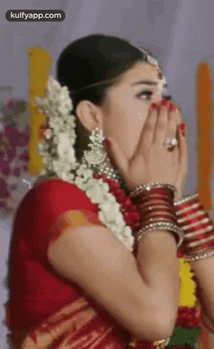 a bride is covering her face with her hands while wearing a red sari .