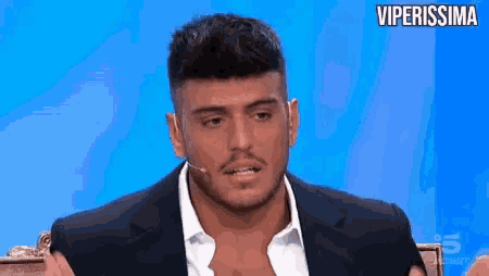 a man in a suit and white shirt is sitting in front of a microphone on a television show .